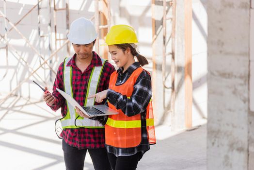 Asian engineer foreman worker man and woman working at building construction site use laptop and talking with radio, engineering hold computer and radio discuss and control worker employee to building