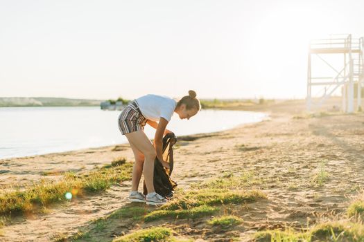 Young female volunteer satisfied with picking up trash, a plastic bottles and coffee cups, clean up beach with a sea. Woman collecting garbage. Environmental ecology pollution concept. Earth Day.