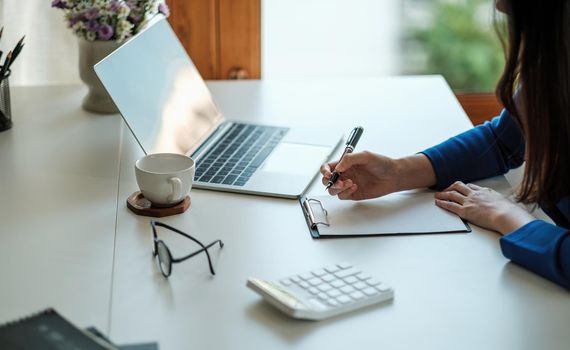 Cropped photo of woman writing making list taking notes in notepad working or learning on laptop indoors- educational course or training, seminar, education online concept.