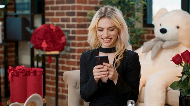 Attractive girlfriend holding smartphone talking with remote boyfriend taking selfie for him enjoying valentine day present during romance anniversary. Beautiful blonde woman surrounded by floral gift