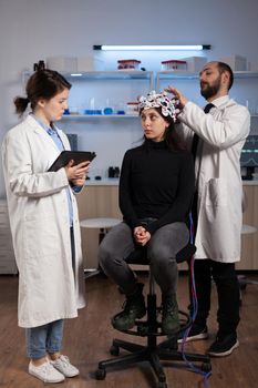 Scientist doctor explaining neurology disease symptoms to woman patient while neurologist researcher adjusting eeg headset during neuroscience experiment in lab. Specialist analyzing brain activity