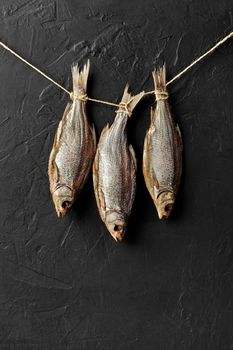 Three salt-dried roaches hanging on rope on black wall background. Traditional beer snack