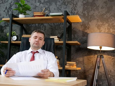 A Tired employee works with financial statements. The man is holding a paper report.