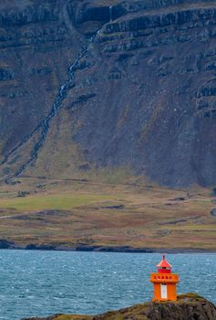 Orange lighthouse near the fjord shore in Iceland, vertical composition