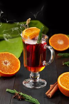 Warming vitamin fragrant tea with orange slices, cinnamon stick, star anise and sprig of fresh rosemary served in glass cup on wooden background