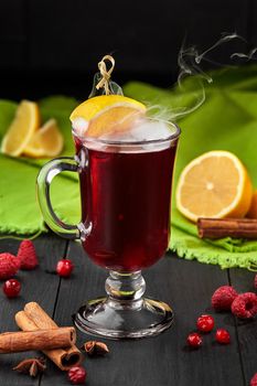 Hot vitamin berry tea from ripe raspberry and cranberry served in glass cup with slice of lemon, aromatic cinnamon stick and star anise on black background