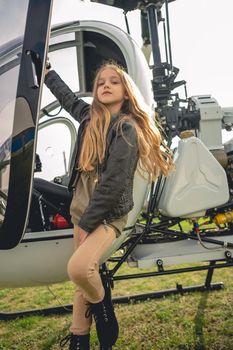 Confident preteen girl with long light brown hair standing on footboard of open helicopter at field of flying club