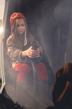 Interested tween girl in aviator hat sitting in modern helicopter, holding control handle. View through glass of cockpit