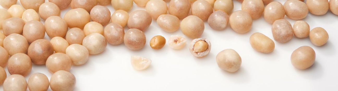 Heap of sweet roasted peanuts in sugar glaze scattered on white surface. Closeup of whole and broken dragees. Popular cracker nuts. Natural food background. Horizontal image with copyspace