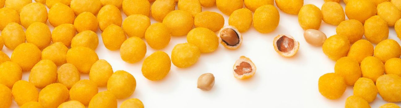 Appetizing roasted peanuts in yellow salty crunchy shell with bacon flavor scattered on white surface. Closeup of whole and broken glazed balls. Popular snacks concept. Natural food background