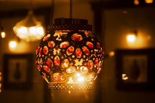 Colorful orient lamp through window on Chinese restaurant. Arabic mystery lantern shining in the cafe. Lights of big city. Atmosphere of comfort and celebration. Selective focus. Blurred background.
