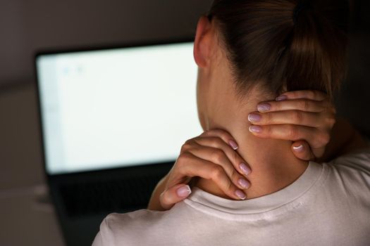 Young woman suffering from neck pain after working on computer. Massaging neck to relieve pain. High quality photo