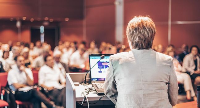 Senior business woman lecturing at Conference. Audience at the lecture hall.