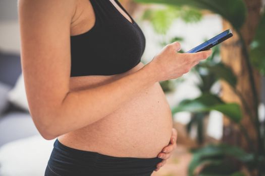 Pregnancy and technoloy supported healthy lifestyle concept. Cheerful happy pregnant woman using smart phone application at home