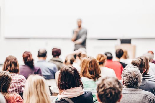 Male speaker giving presentation in lecture hall at university workshop. Audience in conference hall. Rear view of unrecognized participant. Scientific conference event. Copy space on whitescreen.