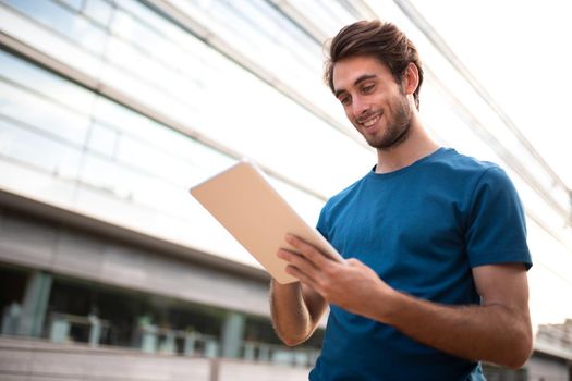 Young caucasian man using digital tablet in business center of city. Copy space. Business and technology concept.