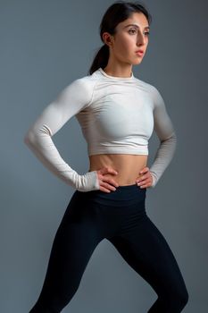 Concentrated sporty young woman doing stretching lunge after intense workout on grey background. Health and sport concept