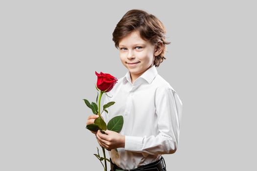 Six years old boy holding a red rose as a gift for his Valentine. Celebrating St. Valentine’s Day or Mother’s Day.