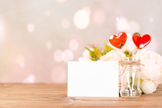 Still life pink Valentines day festive background with empty blank paper card and 2 heart shaped lollipop on wooden table. Mockup with copy space for design.