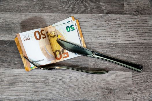 50 euro banknotes with fork and fork on wooden surface