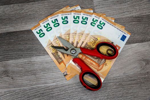 50 euro banknotes with work scissors on wooden surface