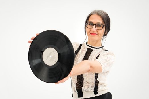 Studio photo of middle aged woman starting getting grey-haired wearing black and white clothes with vinyl record in hands on white background, middle age sexy lady, happy life concept.