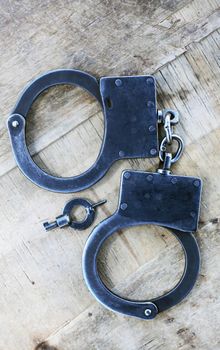 Old metal fastened handcuffs near key on wooden background