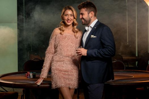 Satisfied stylish attractive young blonde woman and bearded guy standing near gaming table in casino. Leisure, lifestyle, gambling concept