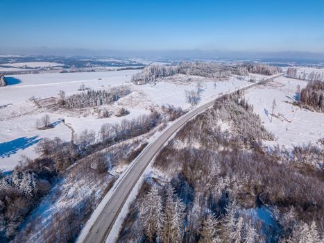 Aerial view of winter road, in sunny day. White frozen and snowy countryside landscape from bird eye, winter theme. Czech Republic, Vysocina region highland