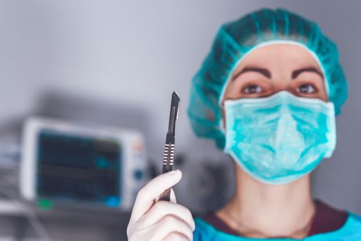Adult woman in medical mask and hat and with scalpel looking at camera before performing surgery in hospital. High quality photo