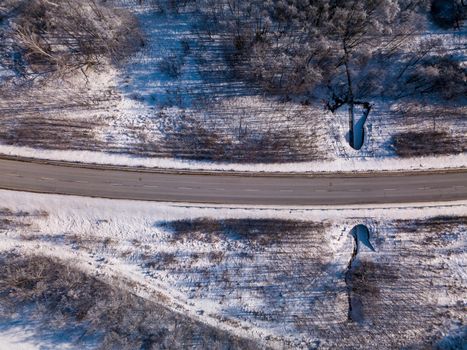 Aerial view of winter road, in sunny day. White frozen and snowy countryside landscape from bird eye, winter theme. Czech Republic, Vysocina region highland