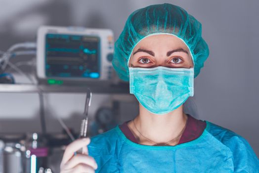 Adult woman in medical mask and hat and with scalpel looking at camera before performing surgery in hospital. High quality photo