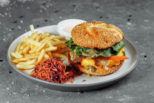 Turkey burger on a bun with cheese, lettuce, tomatoes and fresh cucumber. Burger with cutlet of turkey meat on a gray background with french fries sauce and salad.