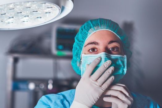 Adult woman in medical mask and hat looking at camera before performing surgery in hospital. High quality photo