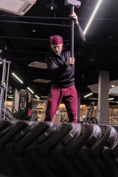 A man hits a sledgehammer wheel in fitness, the concept of a healthy lifestyle male sledgehammer active sledge hammer, In the afternoon gym muscular in adult for bodybuilder concentration, train ethnic. Club dedication man, strenght