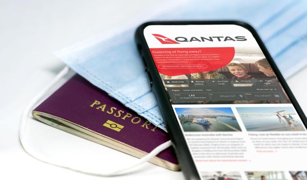 Sydney, Australia, July 2021: phone with the Qantas australian airlines app on the screen lying over a protective mask and a passport. Travel safety and restrictions during coronavirus pandemic