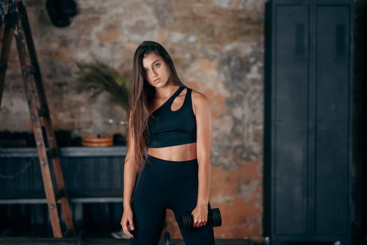 Young woman posing at the camera with dumbbells in her hands in sport gym.