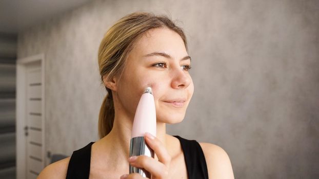 Beautiful young woman is using vacuum device for removing blackheads and acne from the face. Self-massage device. Home cosmetology concept