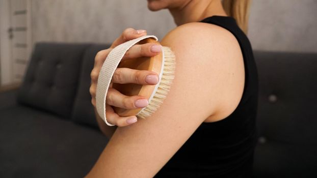 Young woman uses a dry brush to self-massage her arms and shoulders. Self-care of body and skin