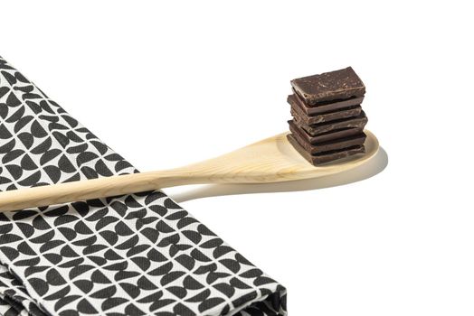 close up of chocolate pieces on wooden spoon with a kitchen napkin on a white background.