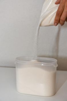 Storing sugar at home, arranging a place in the kitchen. Pouring sugar from a bag into a plastic container.