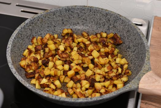 delicious crispy golden fried potato cubes on an old metal frying pan close-up. Cooking homemade fried potatoes in a pan.