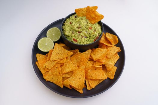 Guacamole sauce and tortilla chips or nachos in black plate isolated on a white background. High quality photo