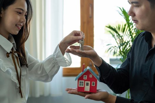 real estate agent holding house key to his client after signing contract agreement in office,concept for real estate, moving home or renting property.