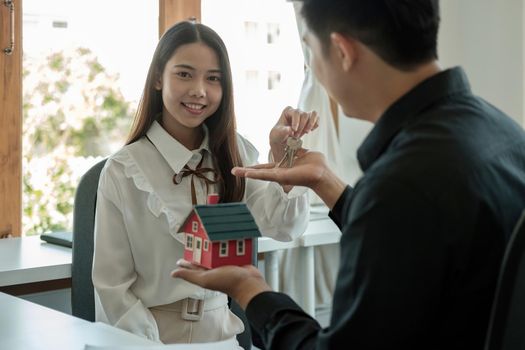 real estate agent holding house key to his client after signing contract agreement in office,concept for real estate, moving home or renting property.