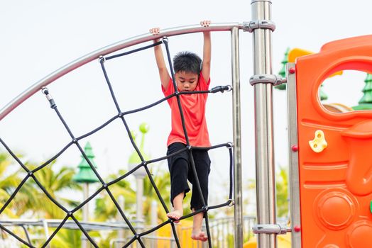 Asian child smiling playing climbing outdoor playground, happy preschool little kid having funny while playing climbs on a rope climbing net on playground equipment in daytime in summer, Little boy