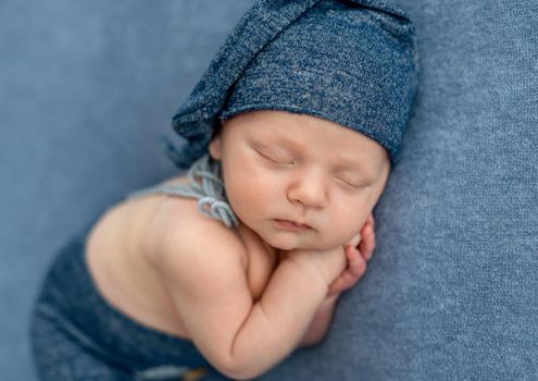 Newborn baby boy wearing knitted hat sleeping and holding hands under his cheeks. Infant kid napping