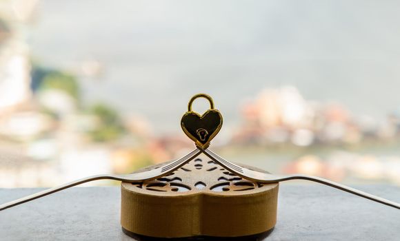 Golden heart shaped love padlock over two intertwined gold forks on Gold heart-shaped box. Valentine's day concept, Copy space, Selective focus.