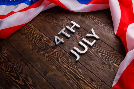 the words 4th july and crumpled usa flag on flat textured wooden surface background.