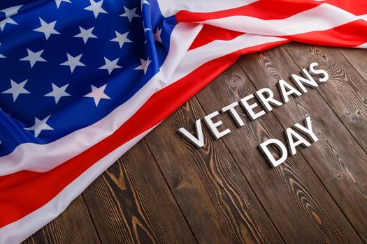 the words veterans day laid with silver metal letters on wooden board surface with crumpled usa flag at upper side with diagonal perspective.